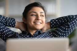 young woman smiling as she leans back from her laptop