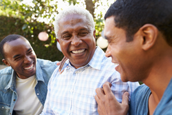 senior man laughs with his two adult sons in the park