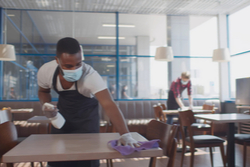 two masked workers clean an empty café during the pandemic