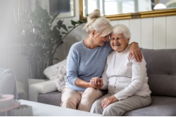 An older mother and her daughter hugging on the couch.
