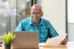 A man reviewing paperwork at his computer.